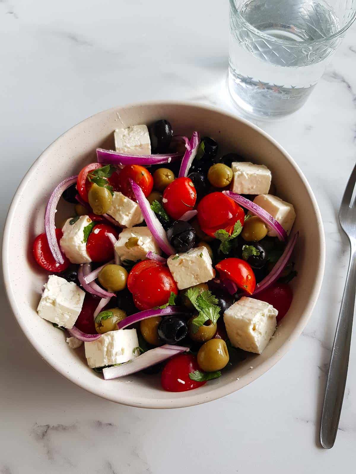 Olive salad in a bowl with a glass of water and a fork on the side.