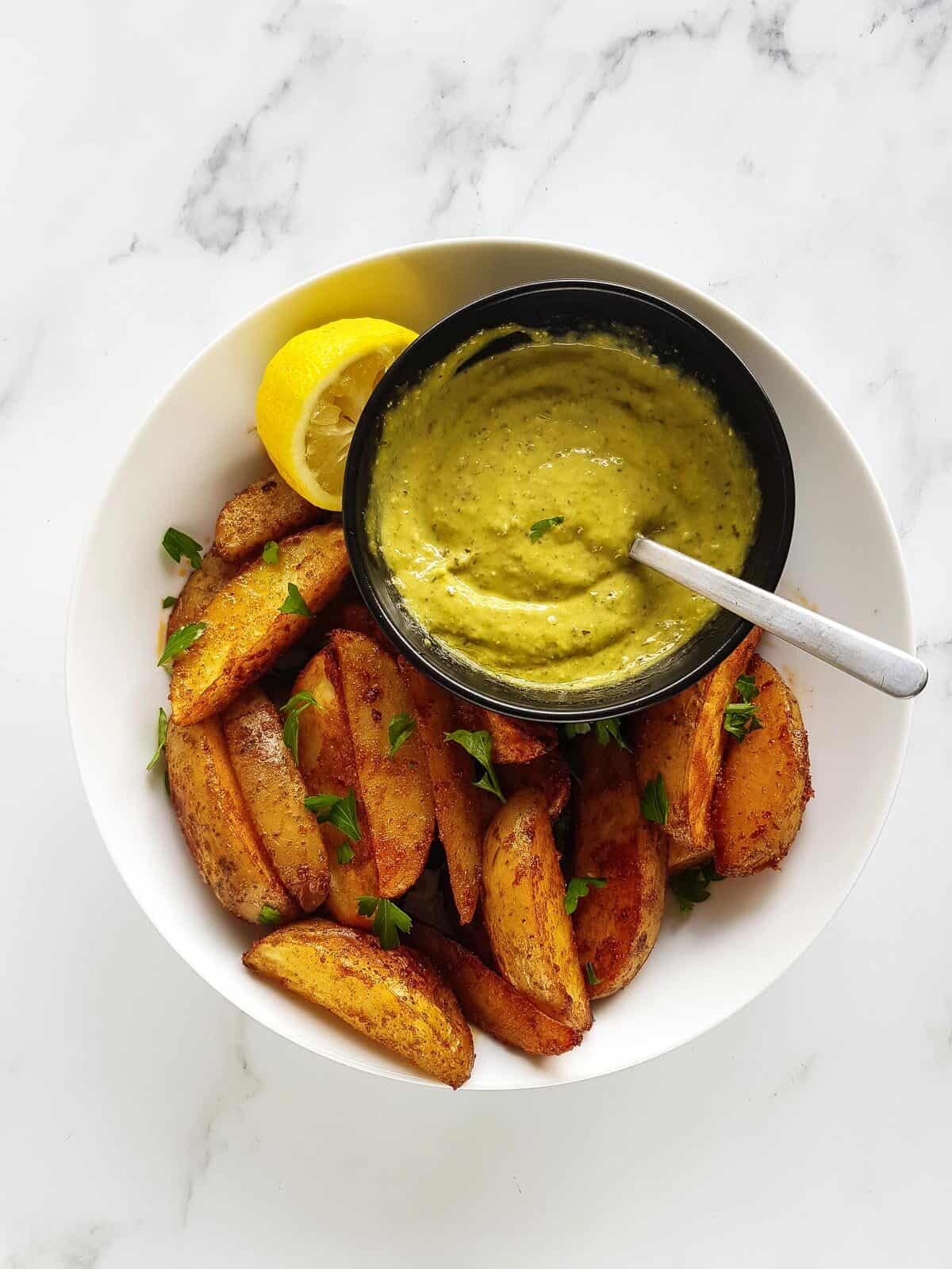 Pesto aioli in a bowl with crispy potato wedges.