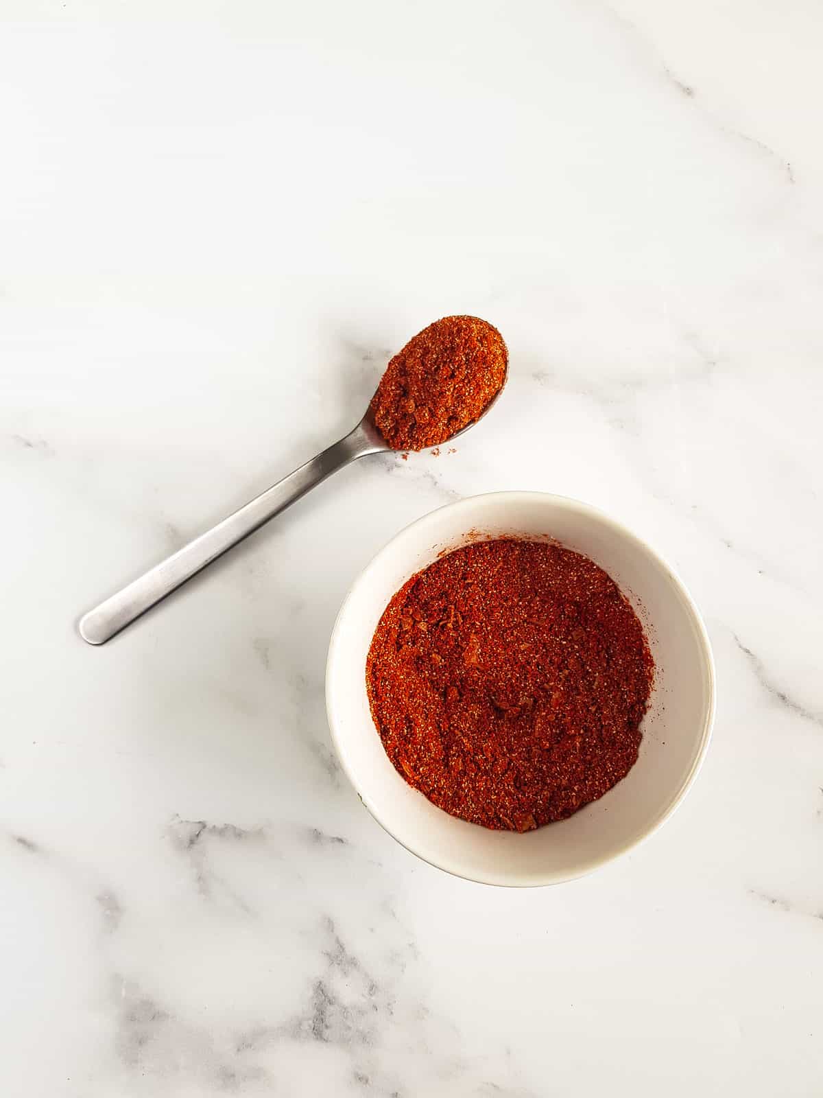 A bowl of pork rub, and a spoon filled with the seasoning next to it.