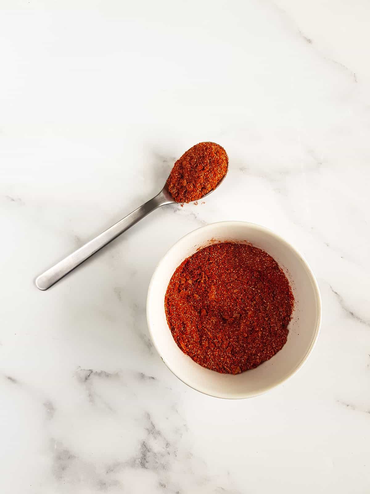 A bowl of pork rub, and a spoon filled with the seasoning next to it.