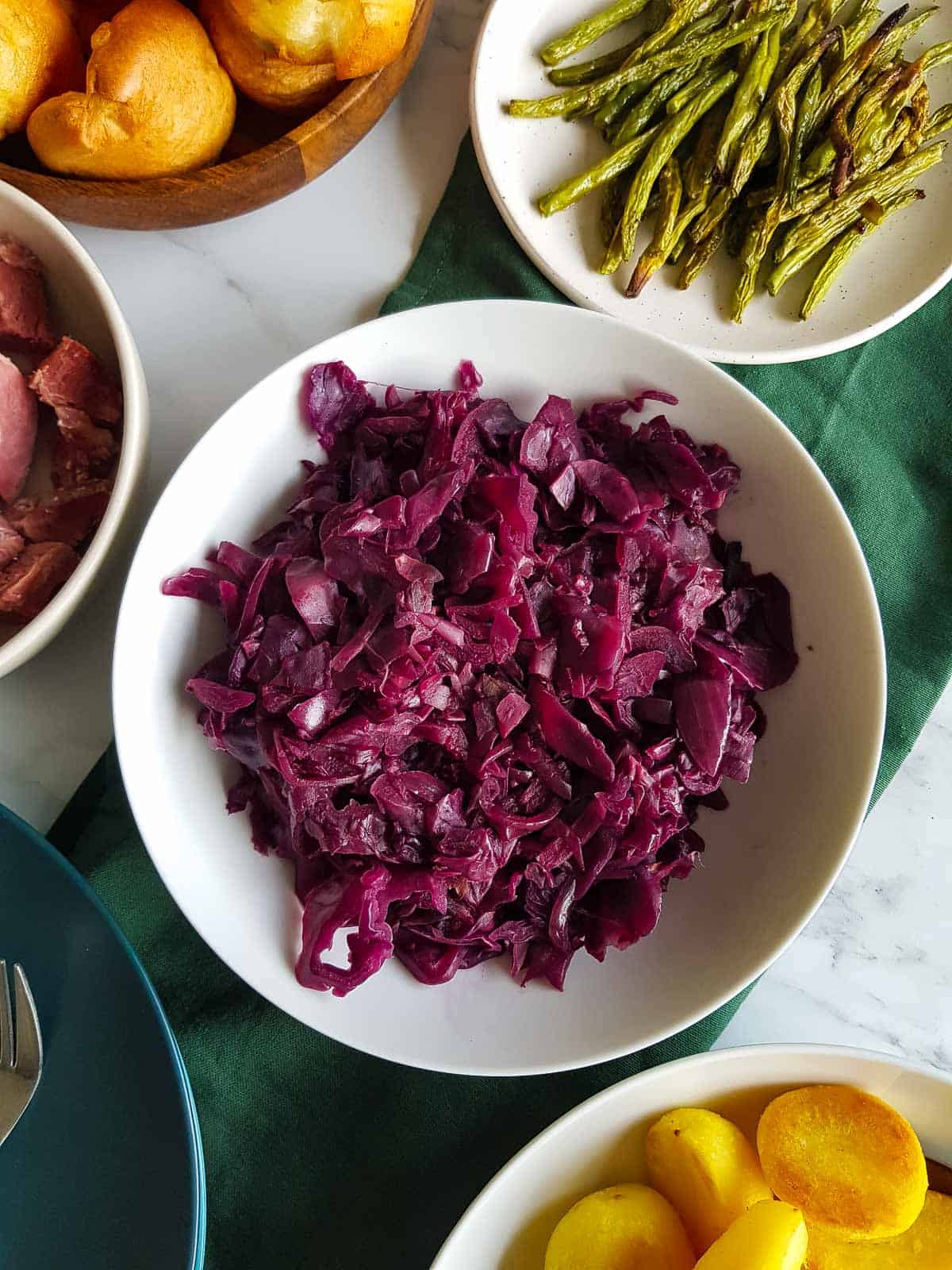 A bowl of slow cooker red cabbage on a table, surrounded by other dishes.