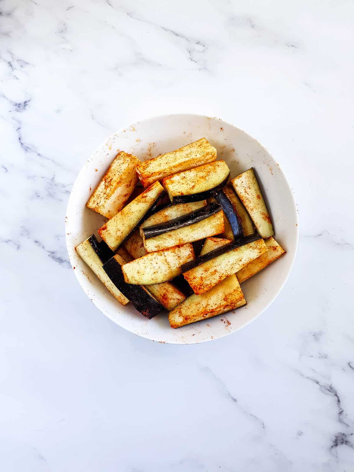 Uncooked, seasoned eggplant pieces in a bowl.