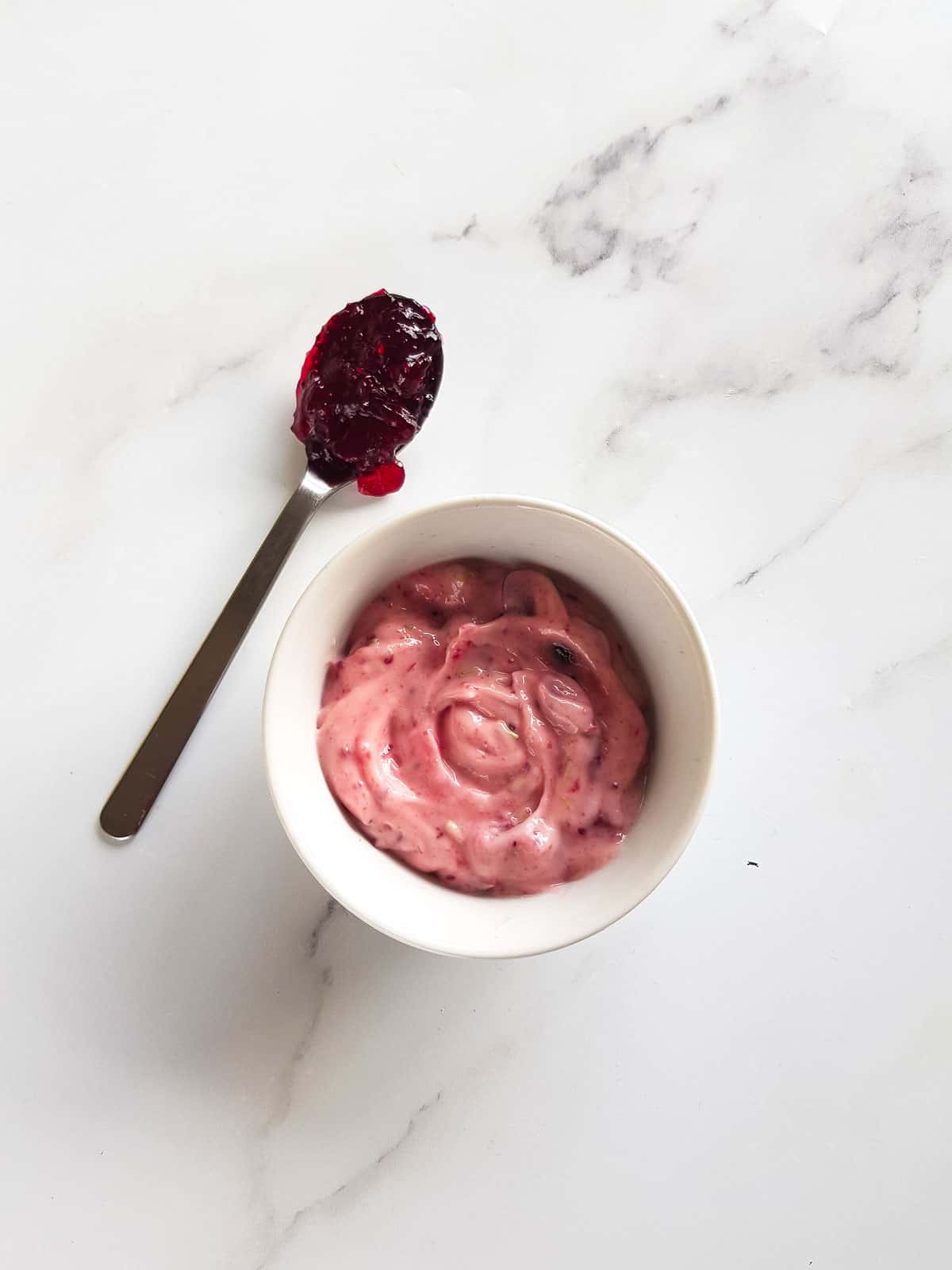 A bowl of cranberry aioli, with a spoonful of cranberry sauce on the side.