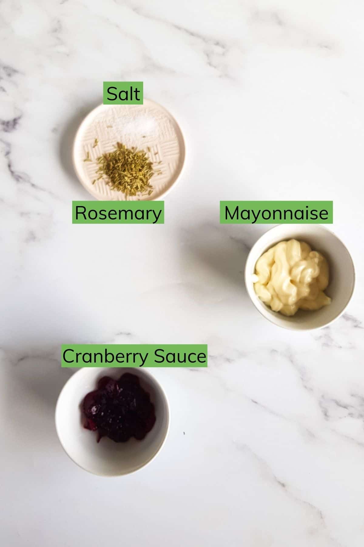 Mayonnaise, cranberry sauce, rosemary and salt on a table.