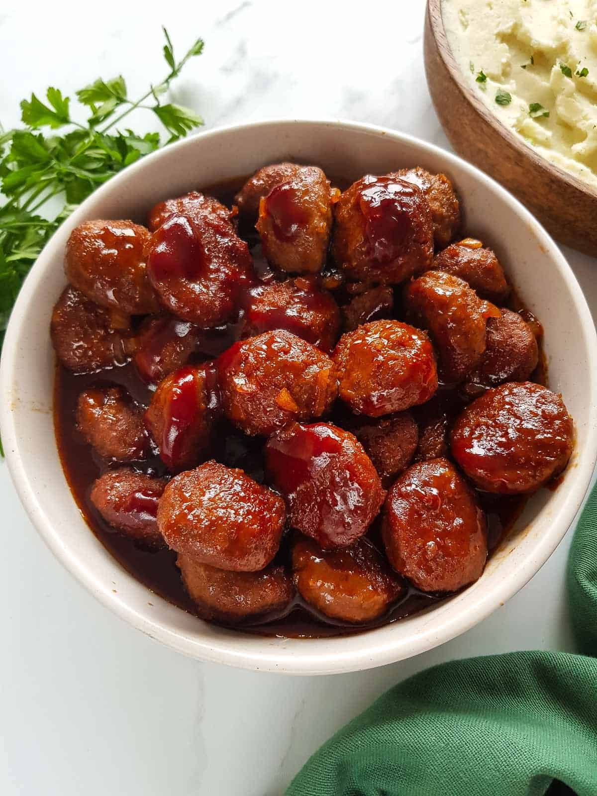 Crockpot BBQ meatballs in a bowl with mashed potatoes in the background.