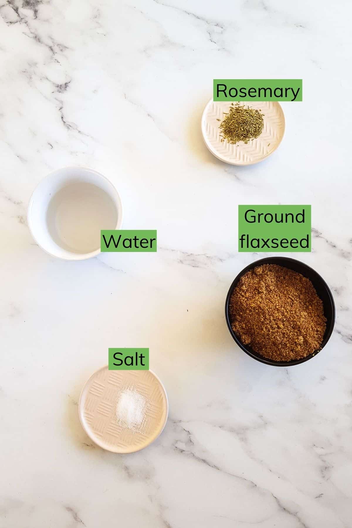 Flaxseed, water, salt and rosemary on a table.