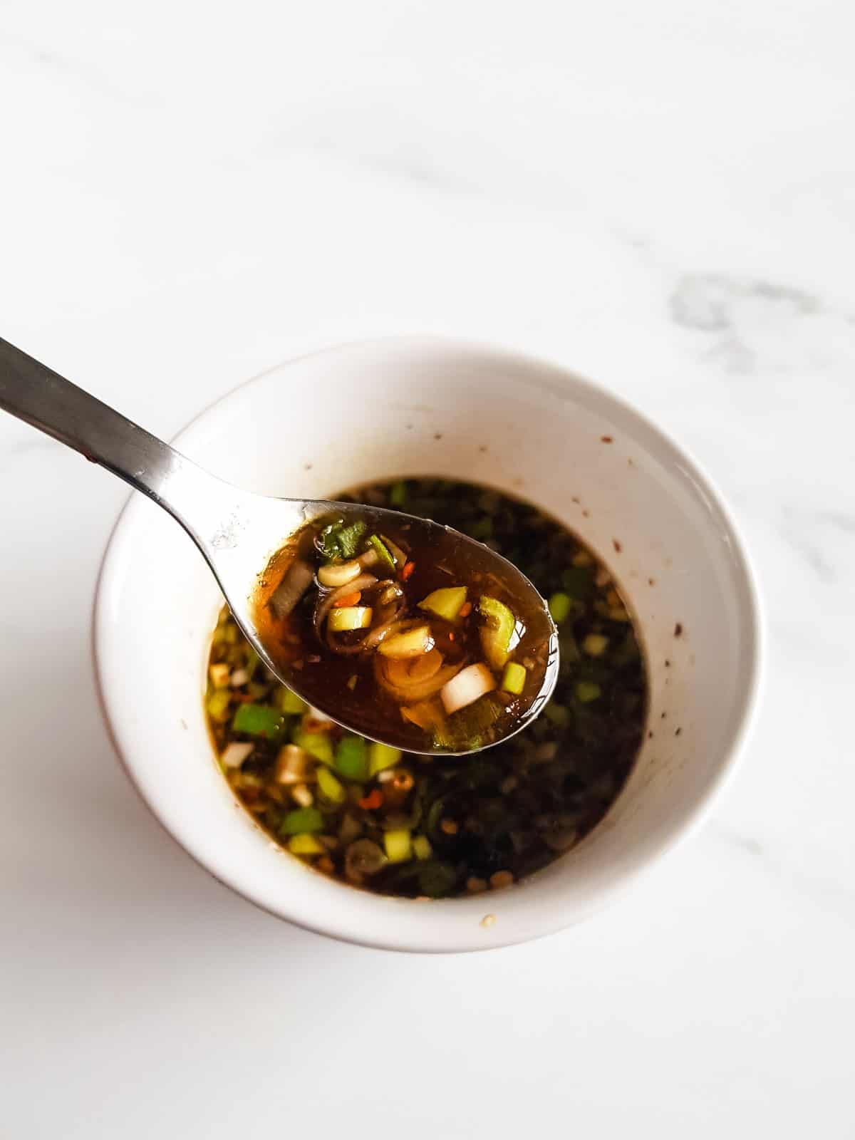 Close up of gyoza sauce, with a spoon lifting up a serving.