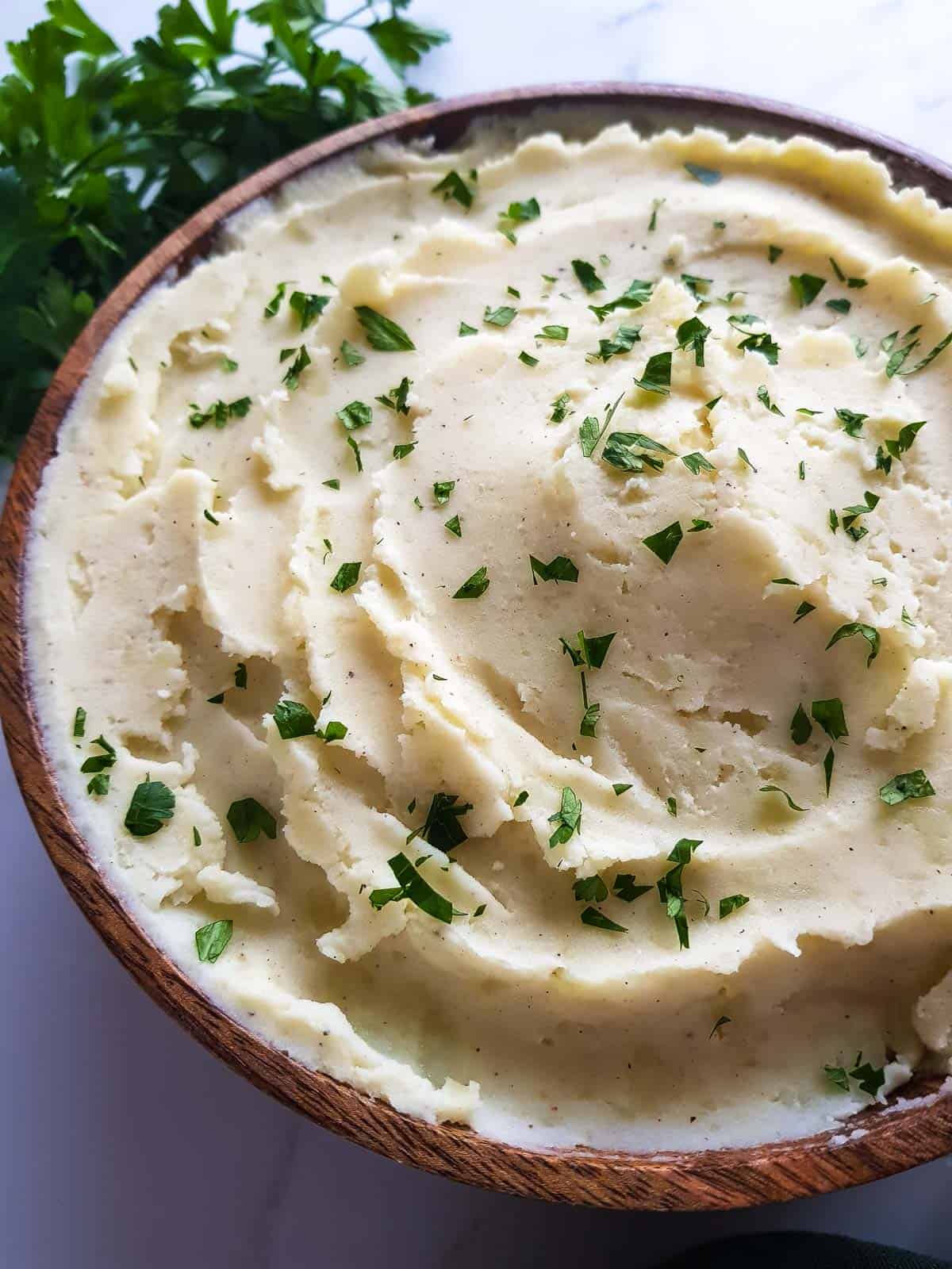 Close up of creamy mashed potatoes in a wooden bowl.