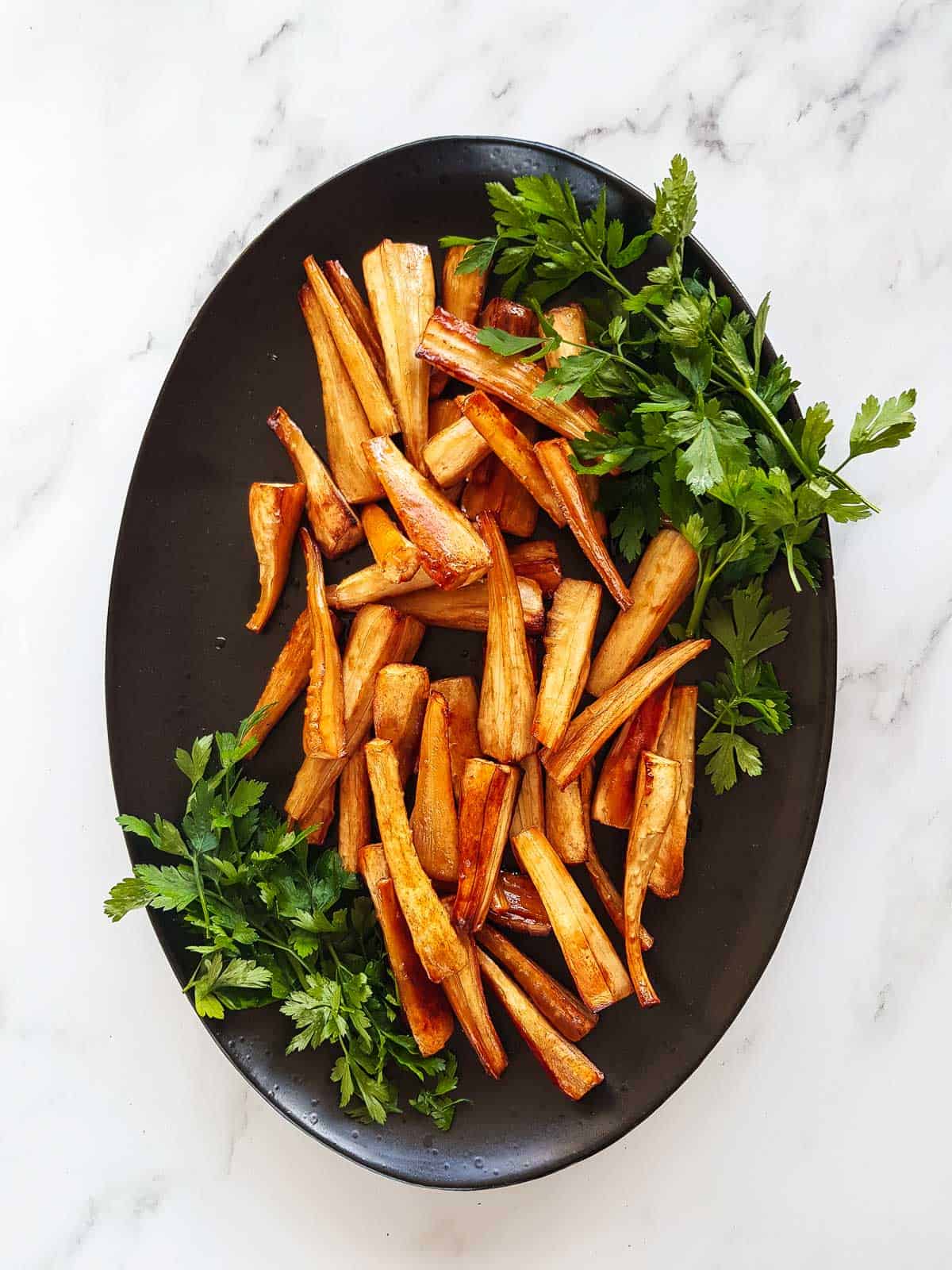 Honey roast parsnips on a serving platter with fresh parsley garnish.