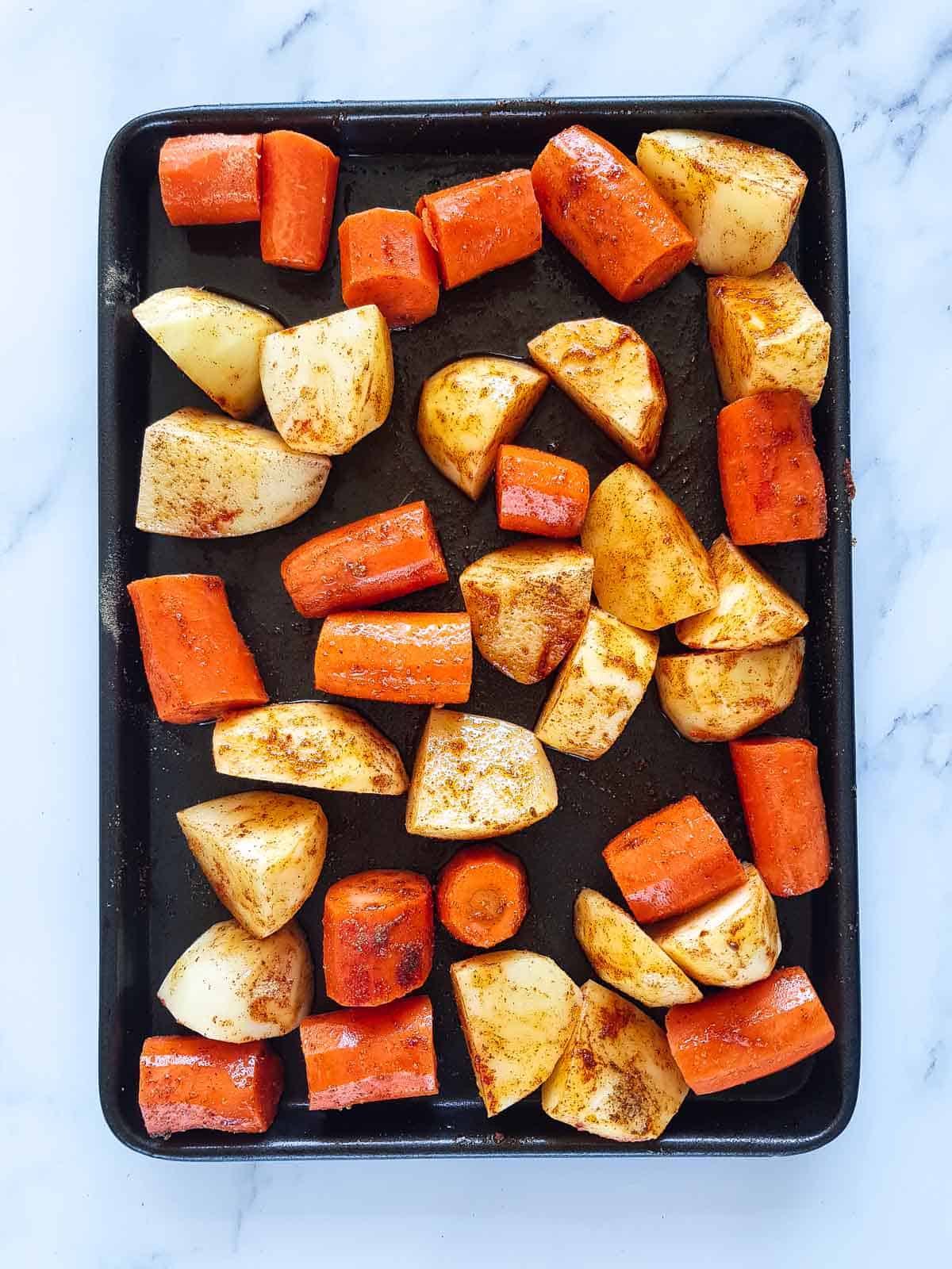 Seasoned carrots and potatoes on a roasting tray.