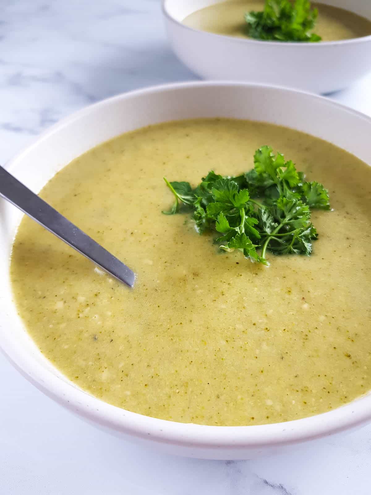 Crockpot broccoli cheese soup in a bowl with a spoon and parsley garnish.