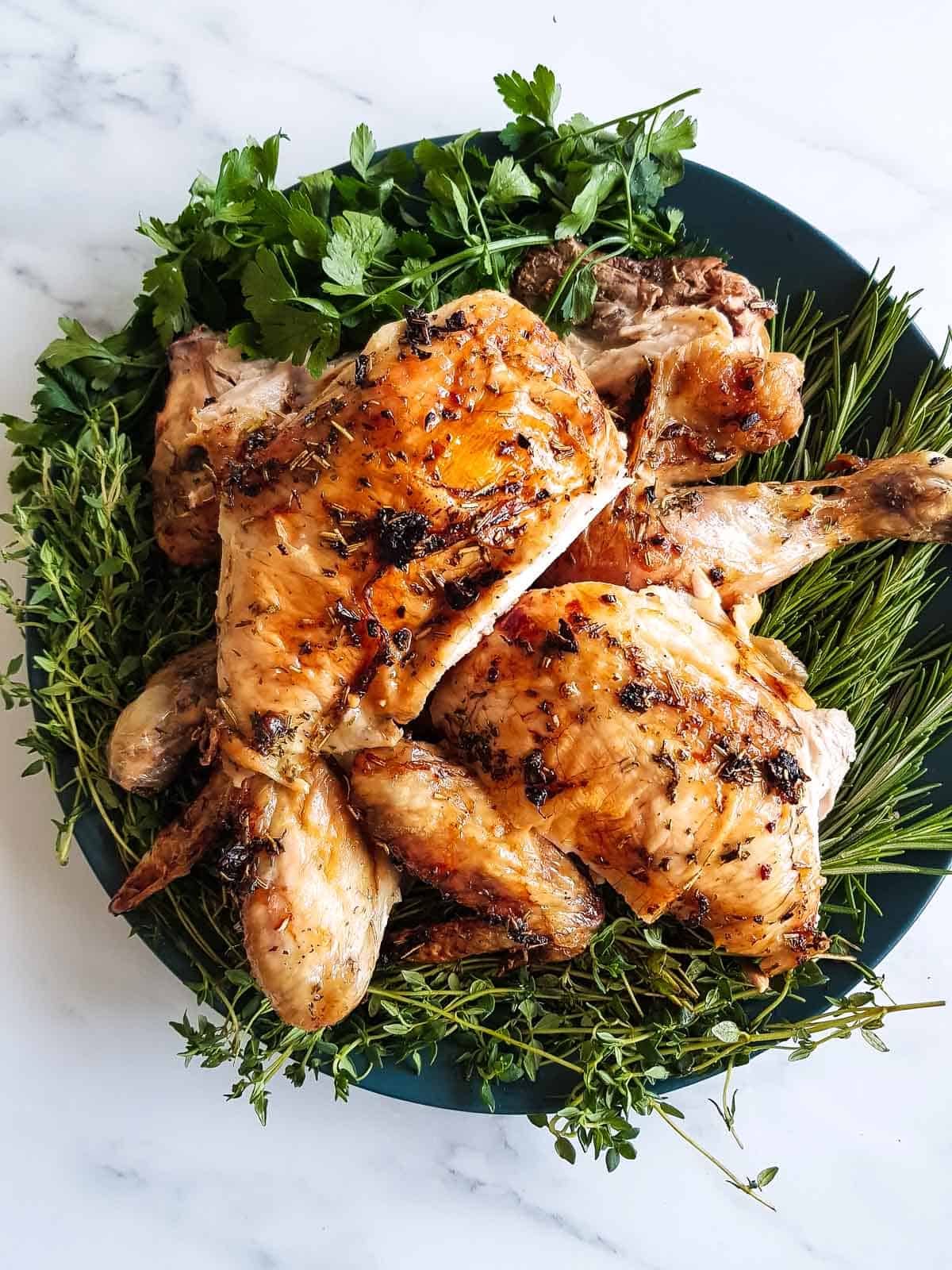 Carved roast chicken on a bed of thyme, rosemary and parsley.