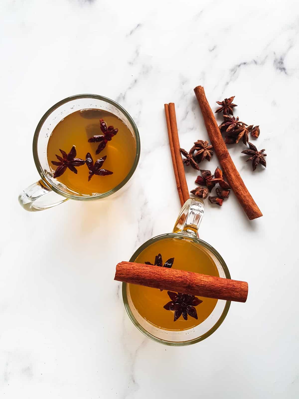 Two cups of star anise tea, with cinnamon sticks and star anise on the side.