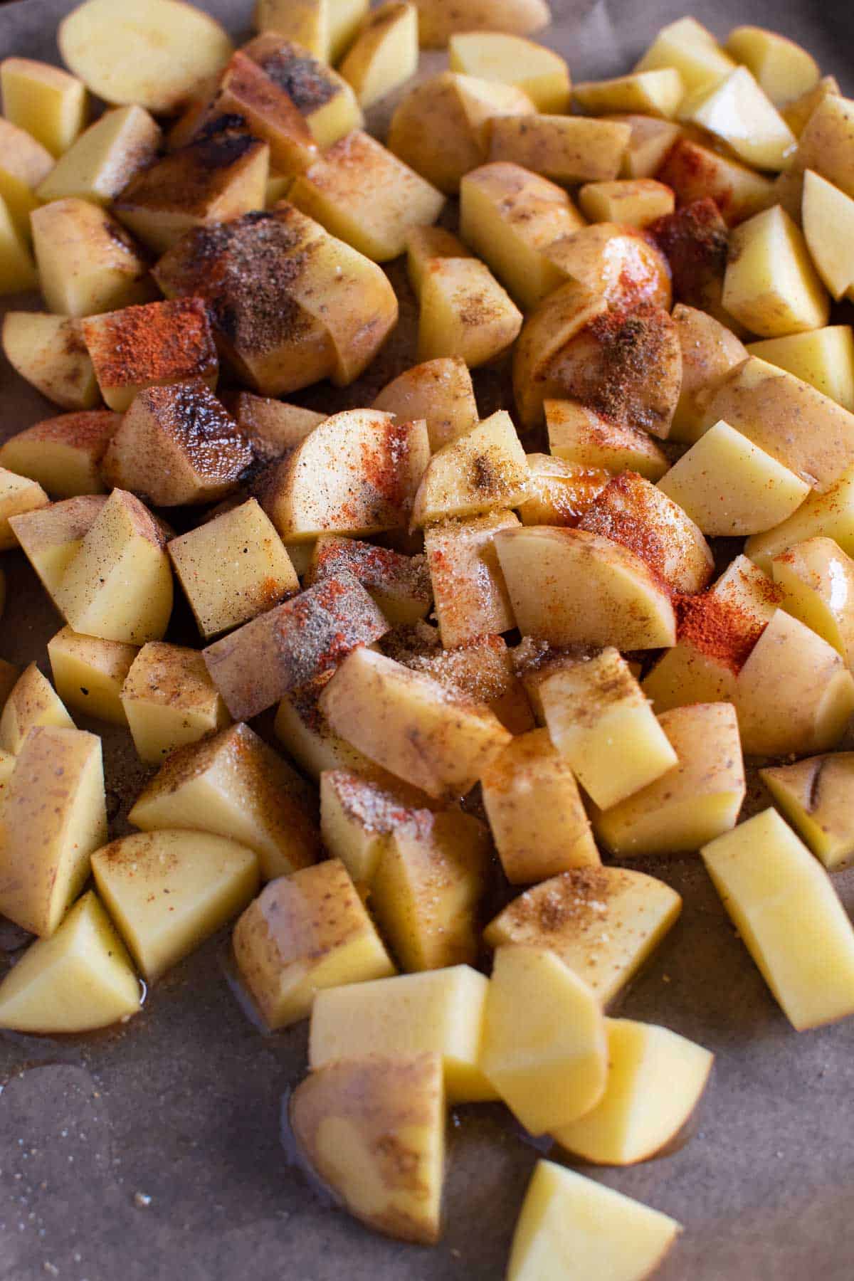 Raw diced potatoes on a baking sheet, covered with olive oil and seasoning.