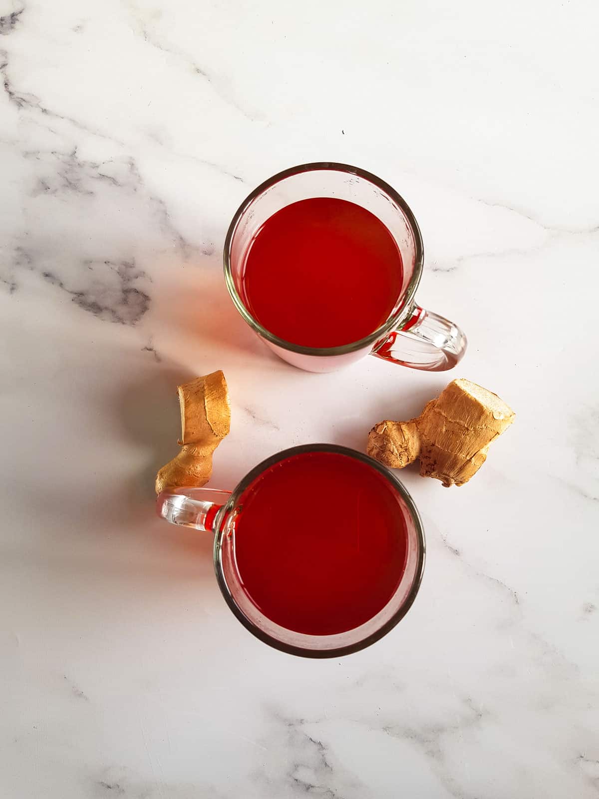 Two cups of ginger turmeric tea with raw ginger on the side.