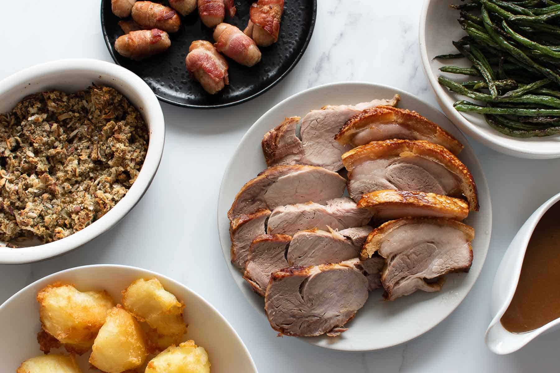 Sliced pork roast on a plate surrounded by side dishes.