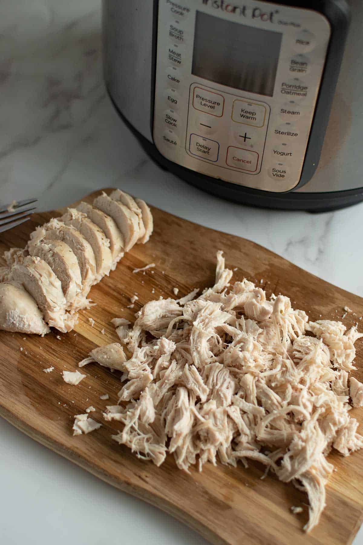 Shredded chicken on a chopping board in front of an instant pot.