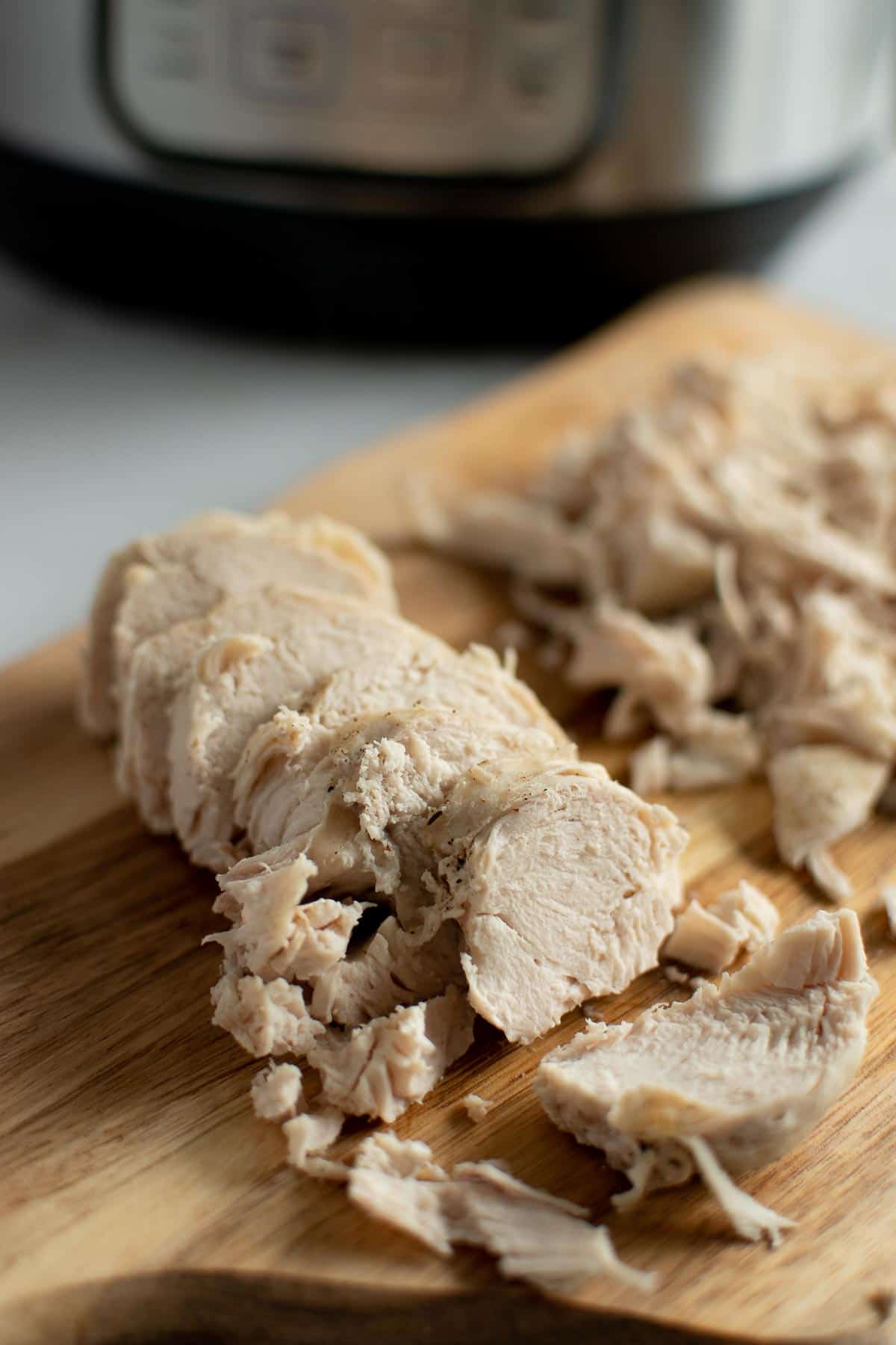 Sliced chicken breast on a chopping board in front of an instant pot.