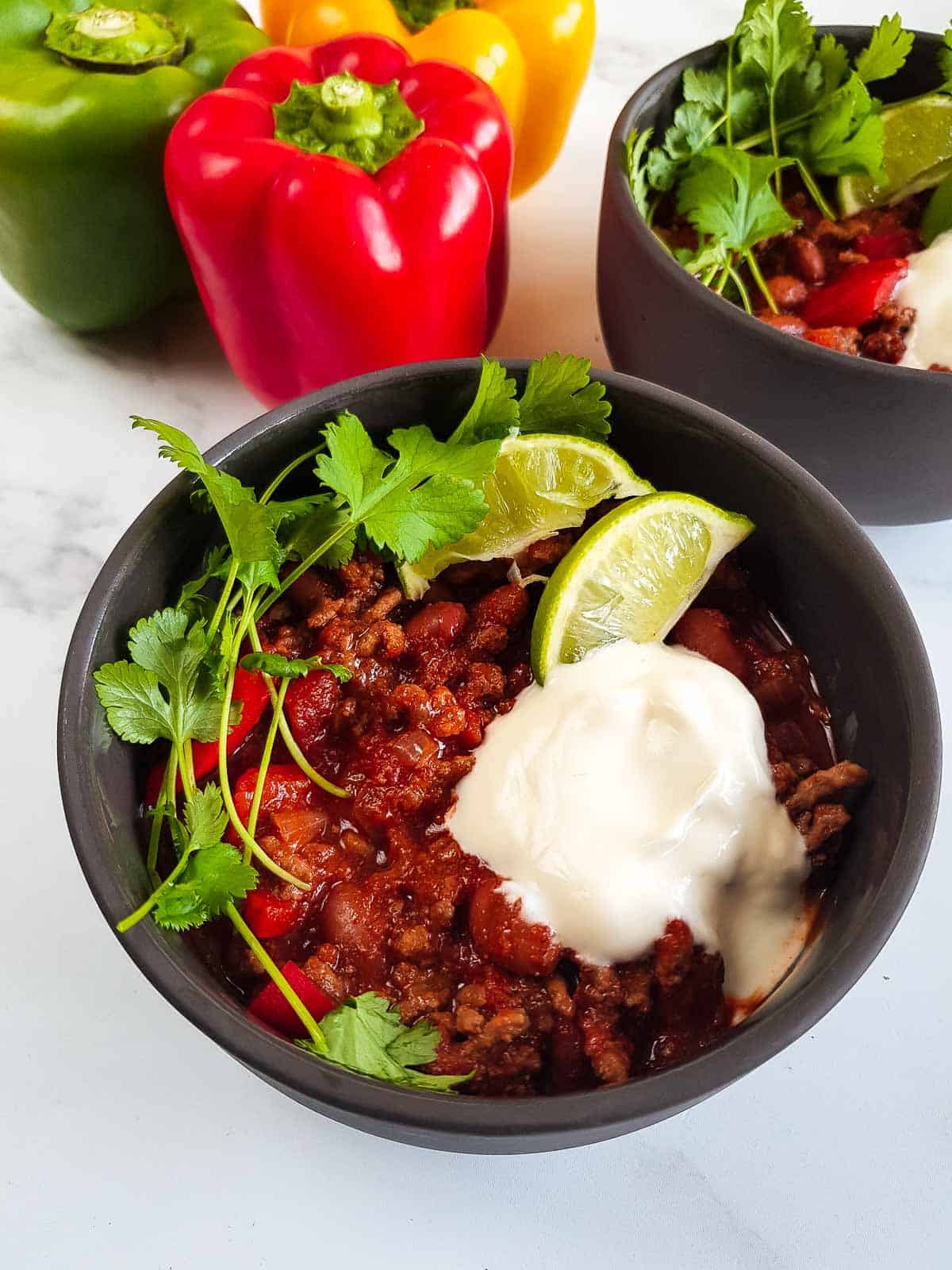Chilli con carne with lime, yogurt and cilantro, with peppers in the background.