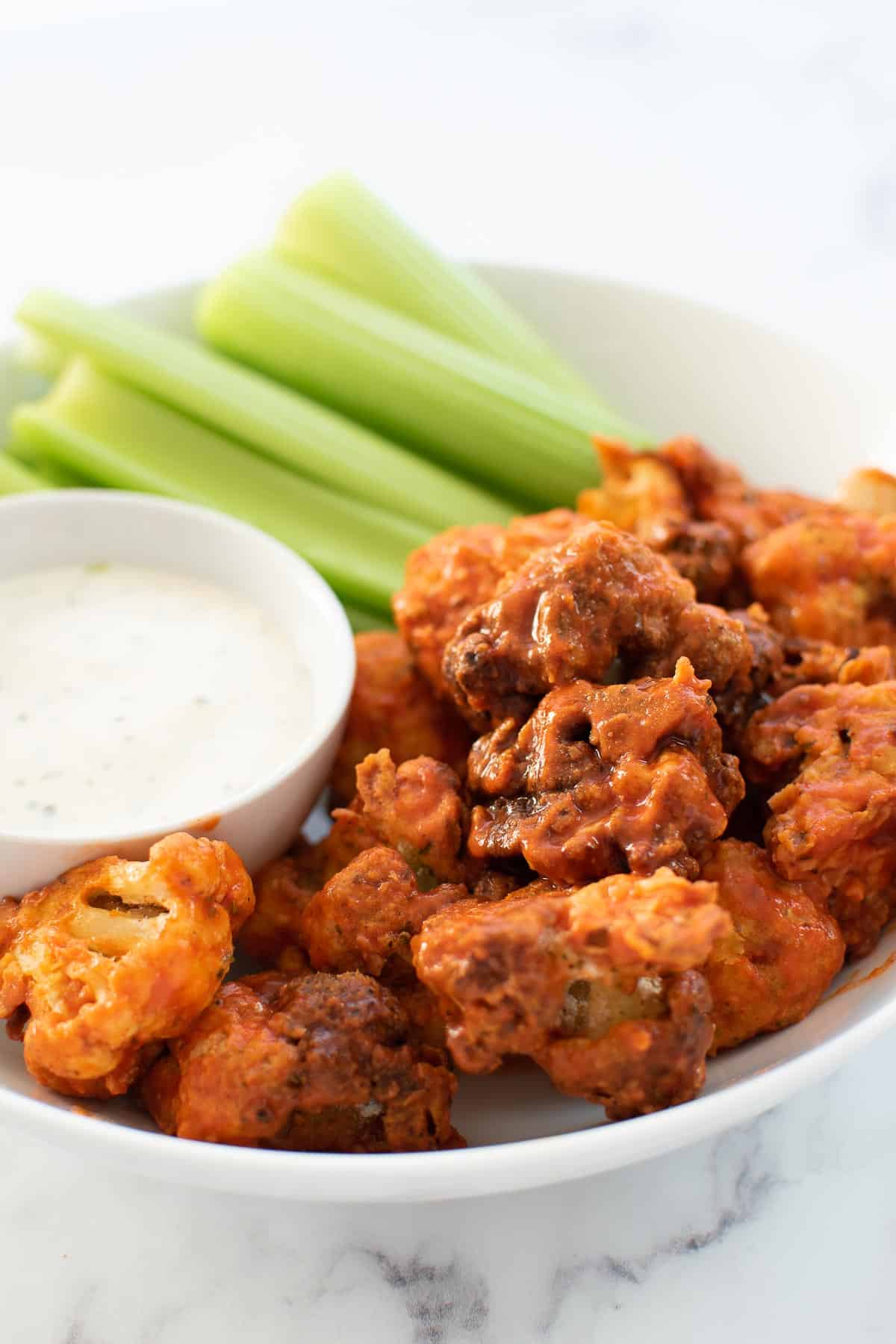 Air fried buffalo cauliflower in a plate with celery and dip.