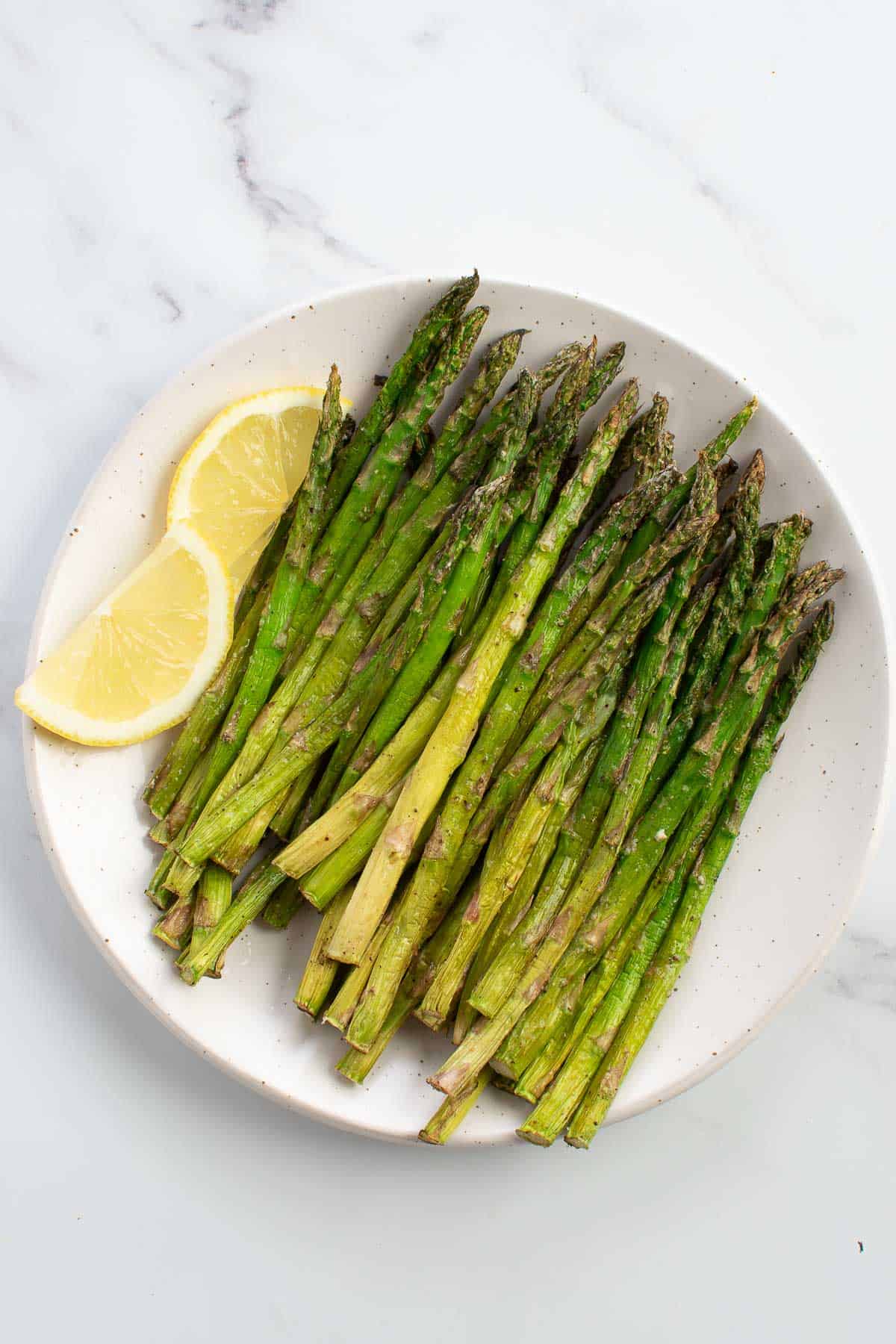 Air Fryer Asparagus on a plate with lemon wedges on the side.