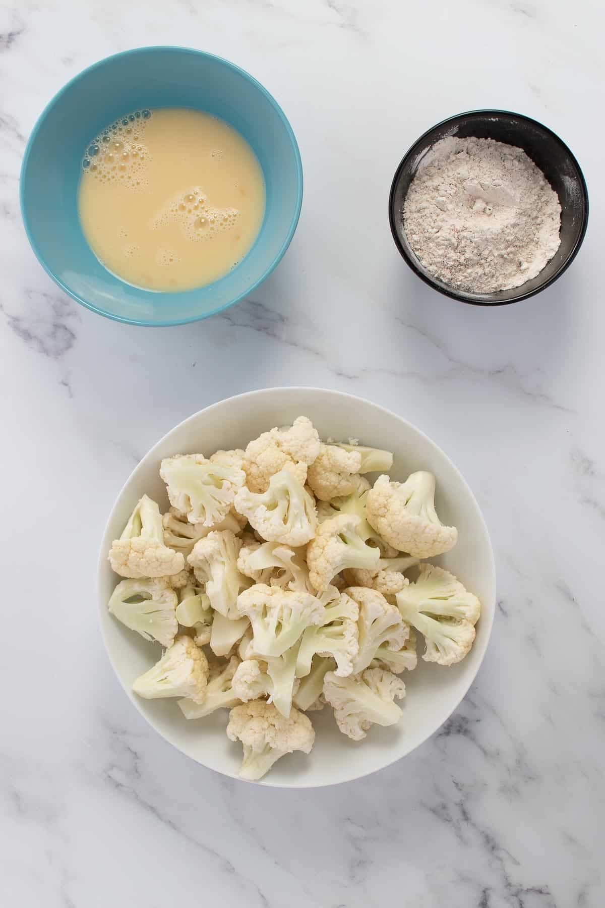 Cauliflower florets, and two bowls of ingredients on a table.