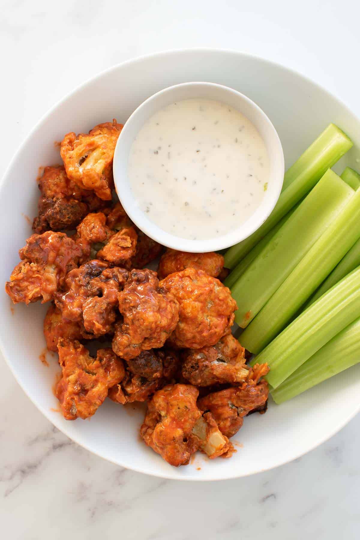 A plate with buffalo cauliflower wings, celery and dip.