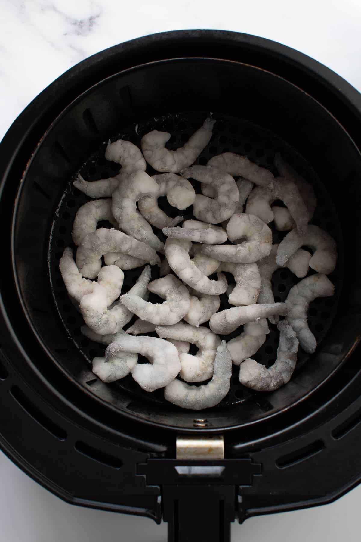 An air fryer with frozen shrimp.