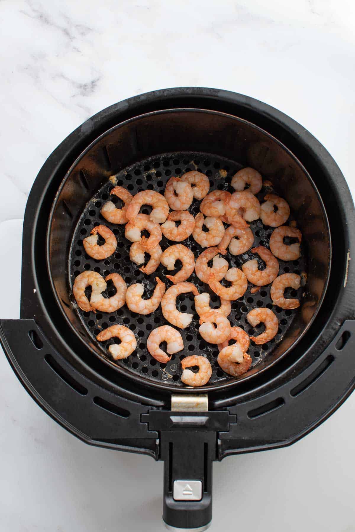 An air fryer with cooked shrimp.