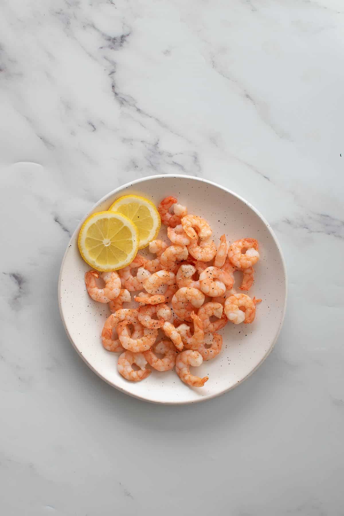 A plate of cooked shrimp with lemon slices.