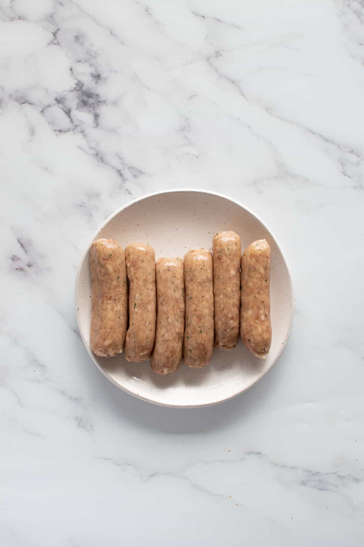 Raw pork sausages on a plate.