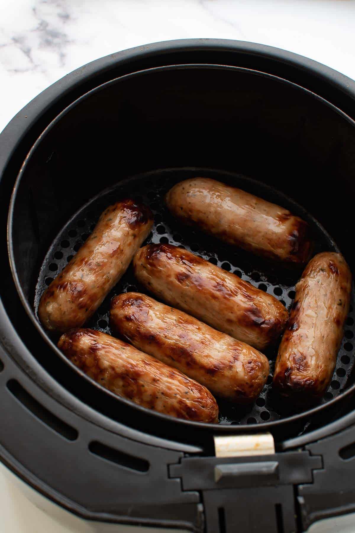 Cooked sausages in an air fryer basket.