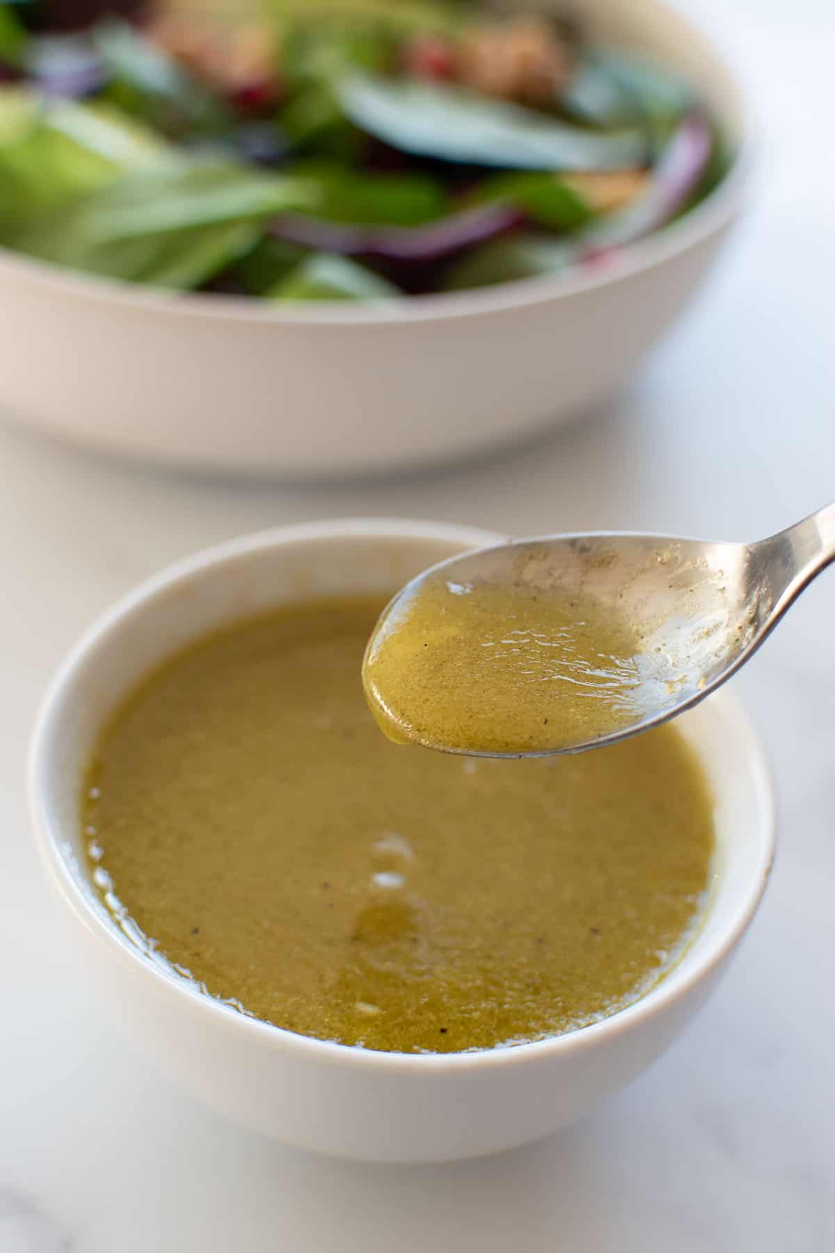 A spoon stirring a bowl of apple cider salad dressing.