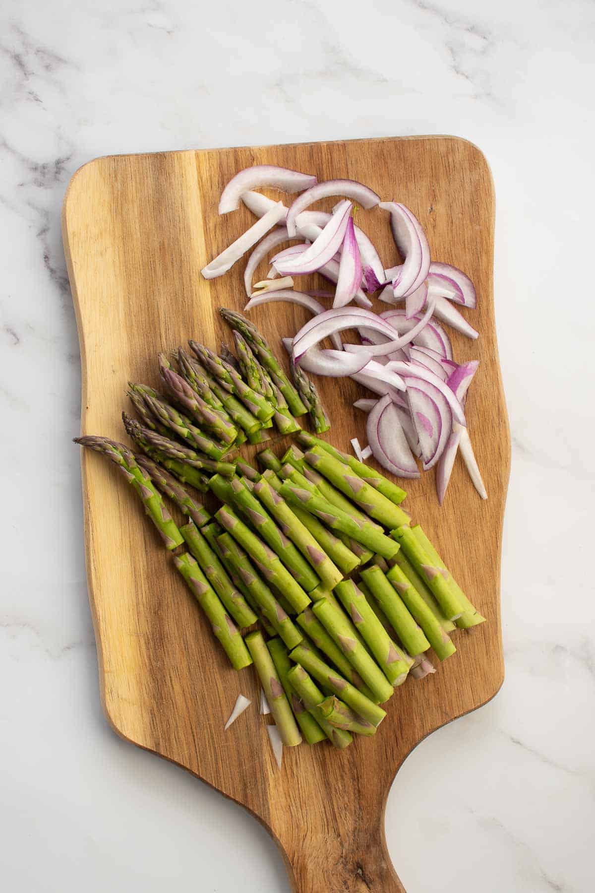 Asparagus and red onion on cutting board.