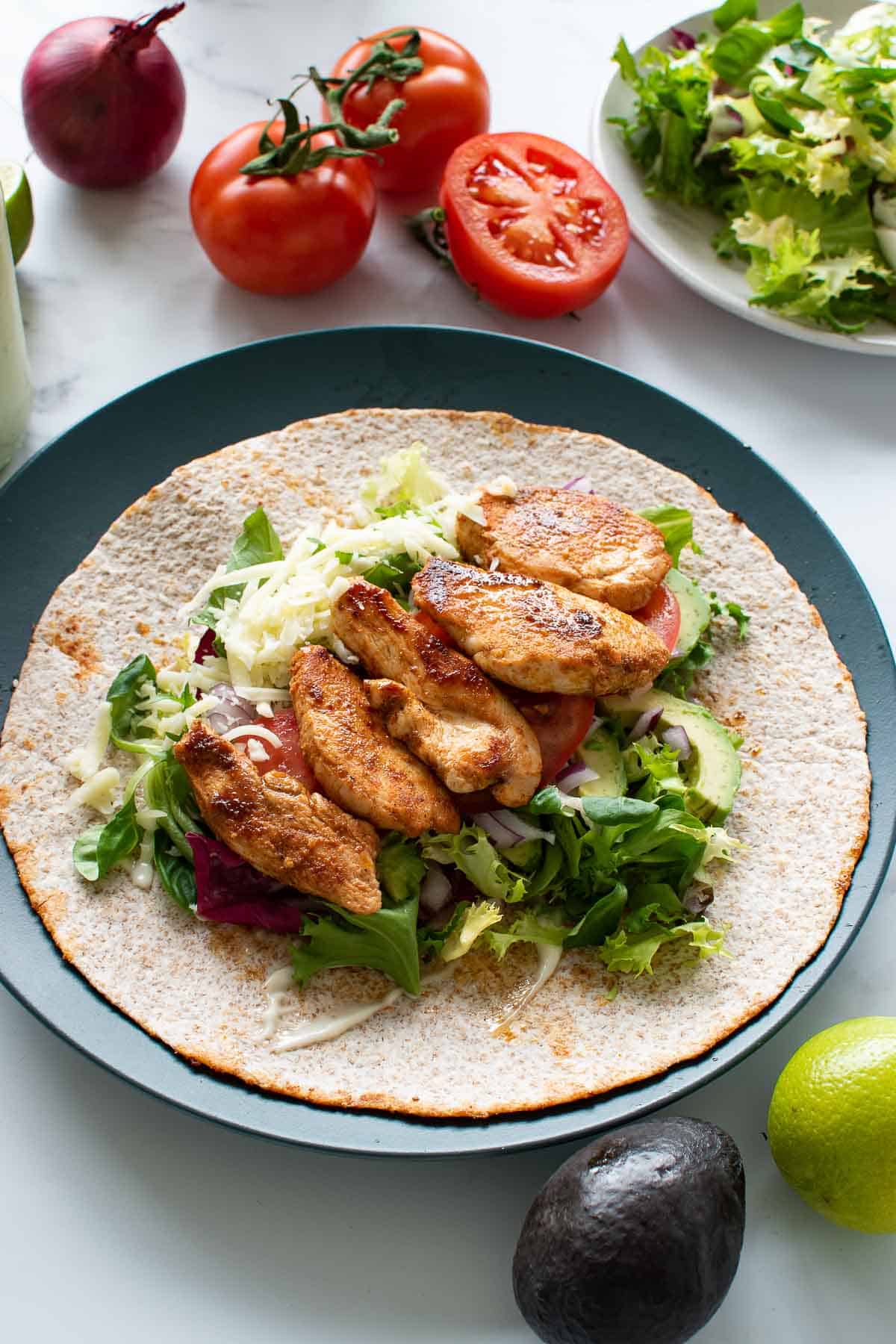 A plate with a chicken wrap, with tomatoes and lettuce in the background.