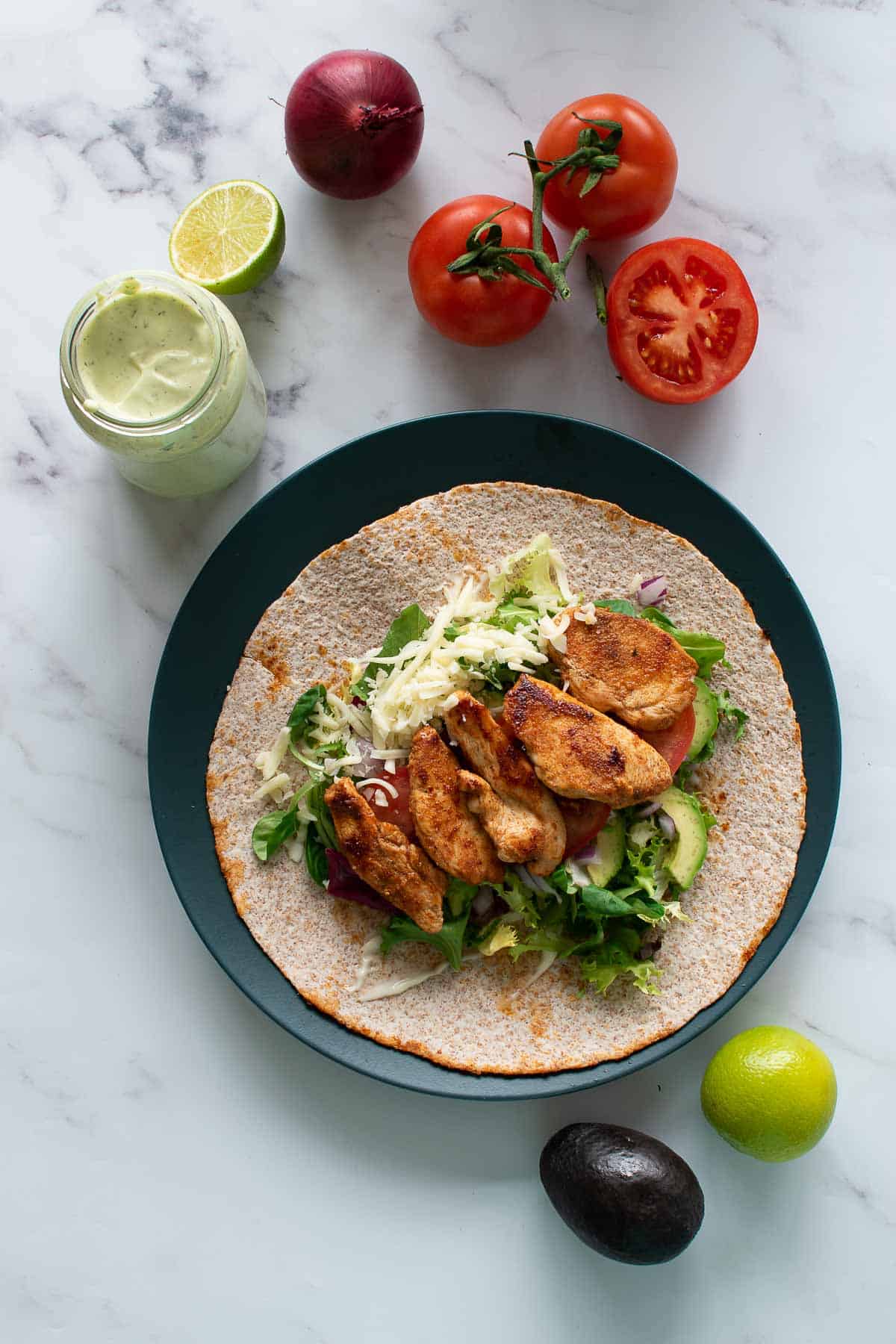 Avocado chicken wraps on a plate, surrounded by vegetables.