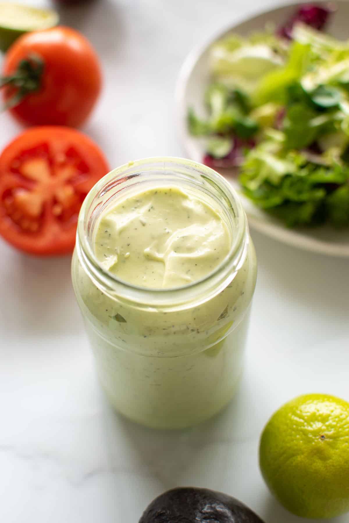 A jar filled with avocado lime ranch dressing, surrounded by vegetables.