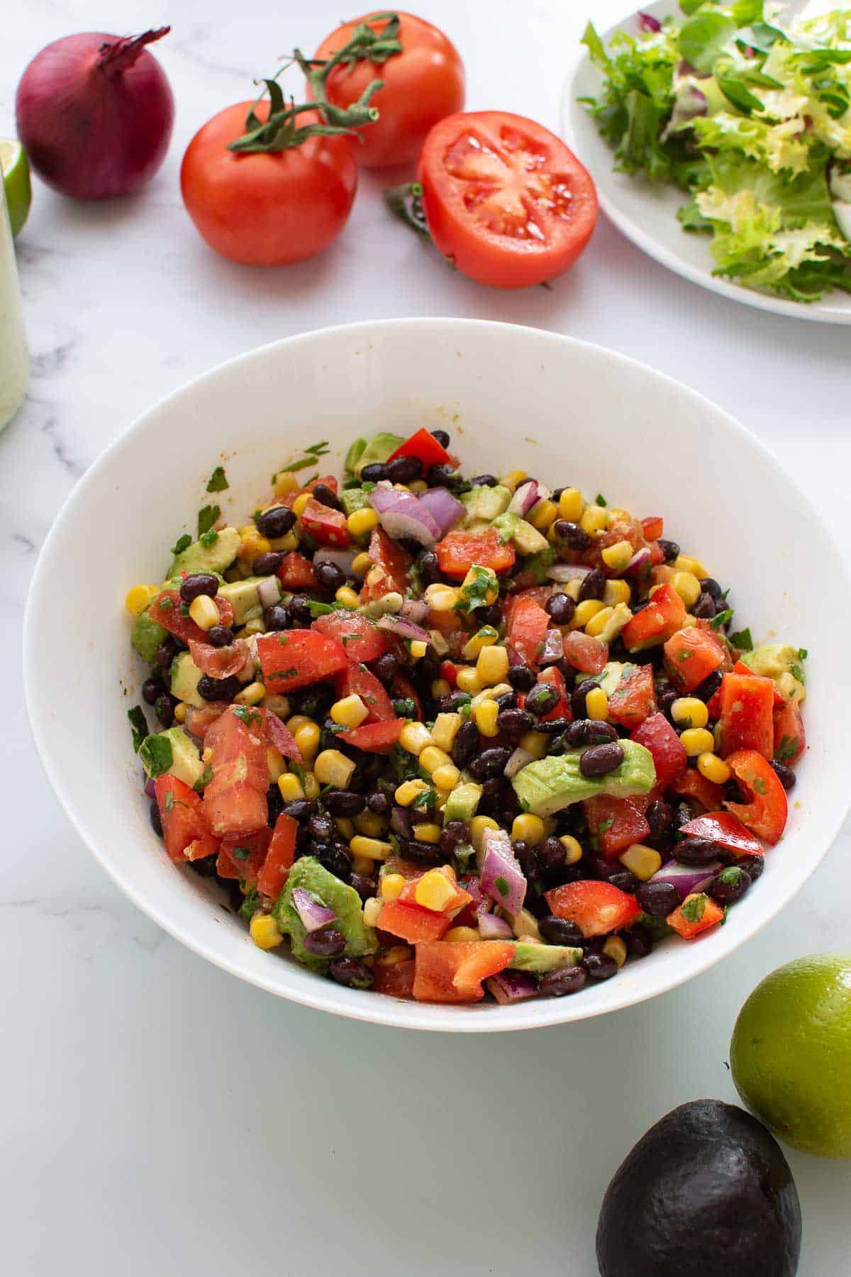 A bowl with black bean corn salad, with vegetables on the side.