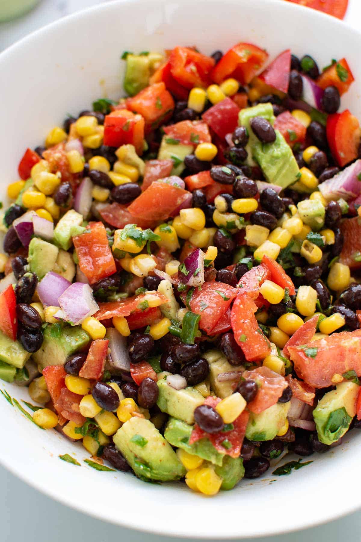 A close up of Mexican salad with corn, avocado, black beans and peppers.