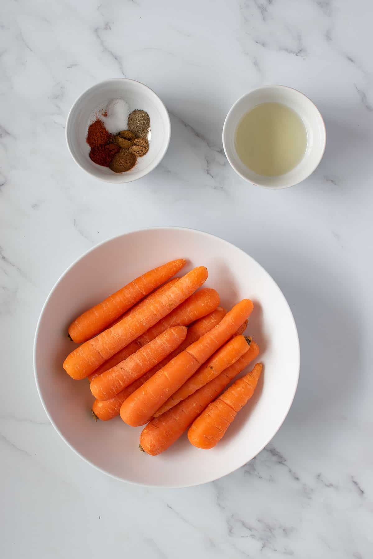 Bowls of carrots, olive oil and spices on a table.