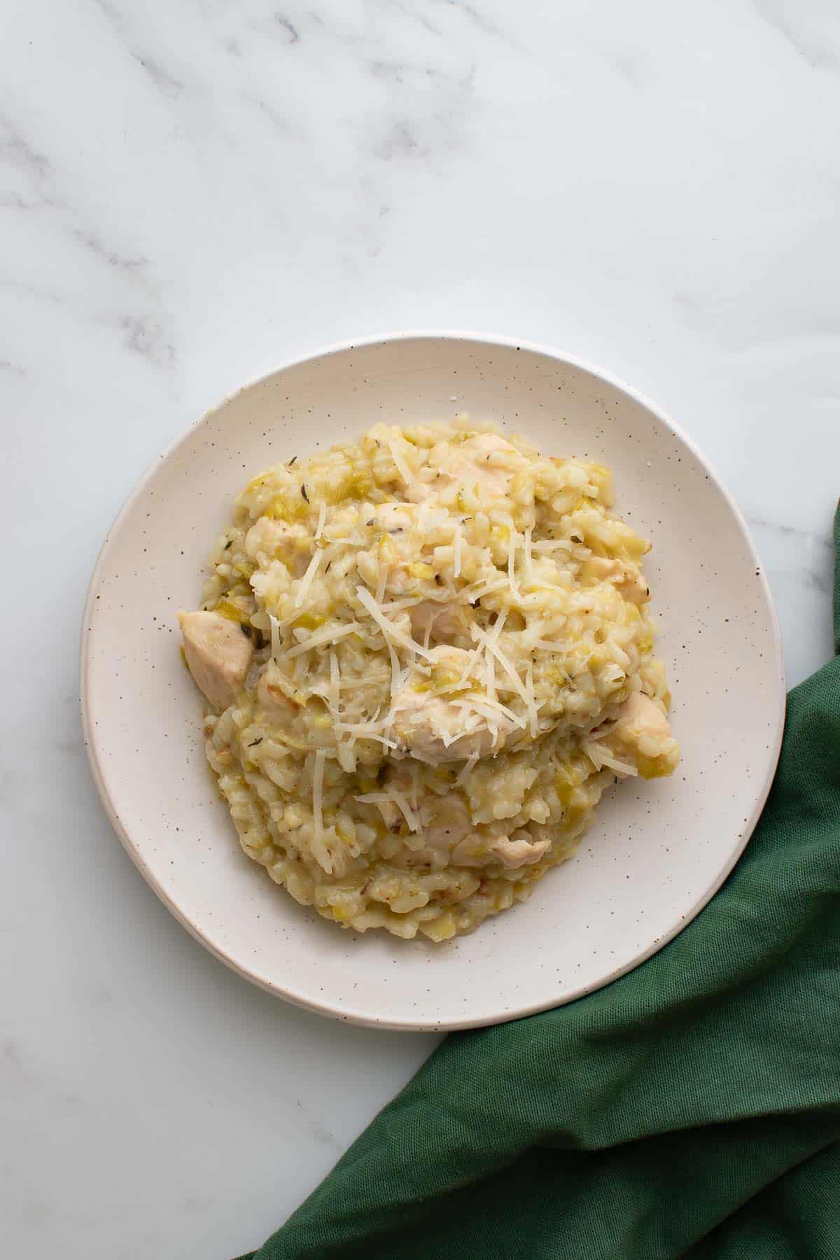 A plate of chicken and leek risotto, with a tablecloth on the side.