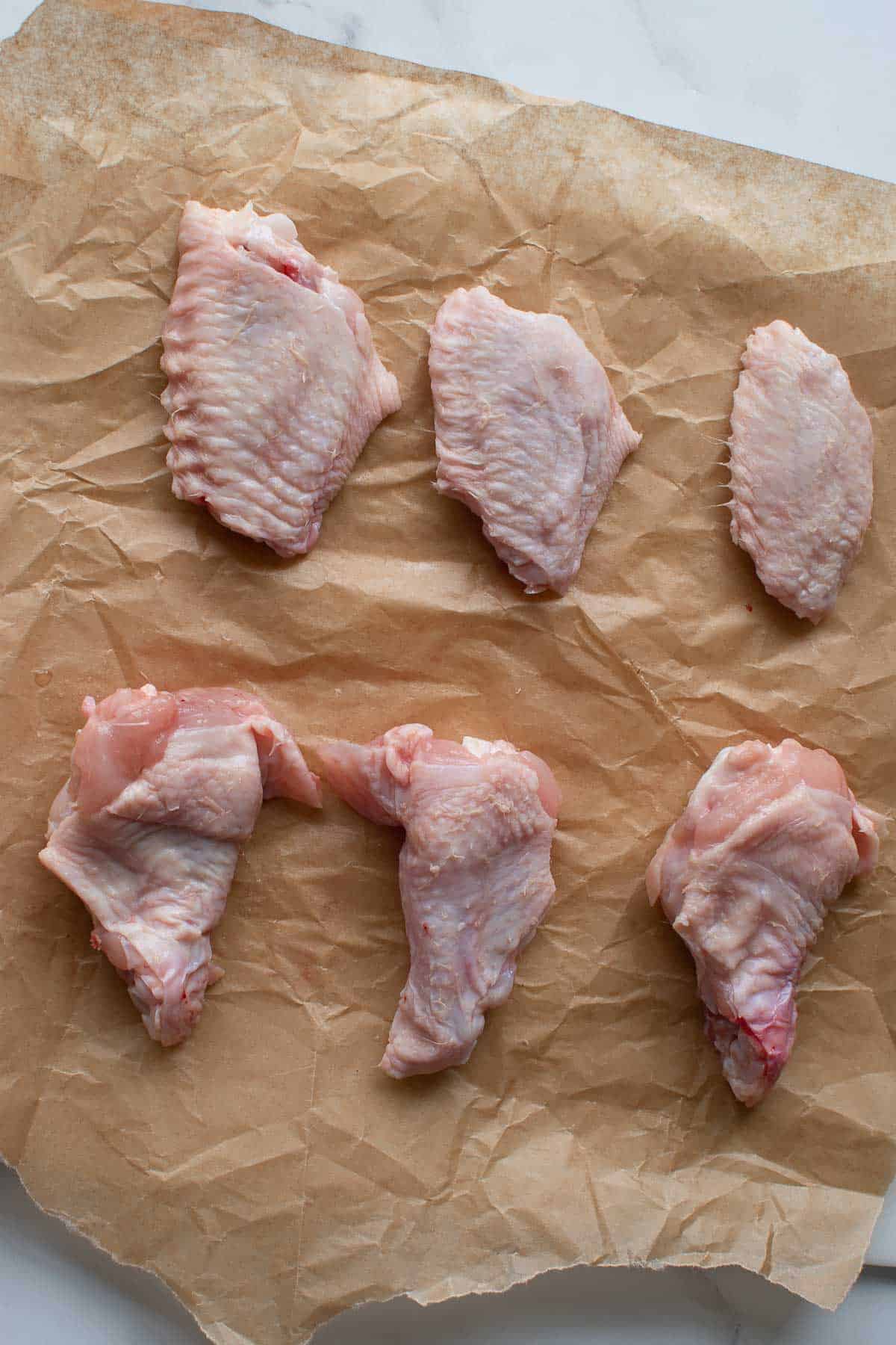 Separated chicken wingettes and drumettes on a parchment paper.