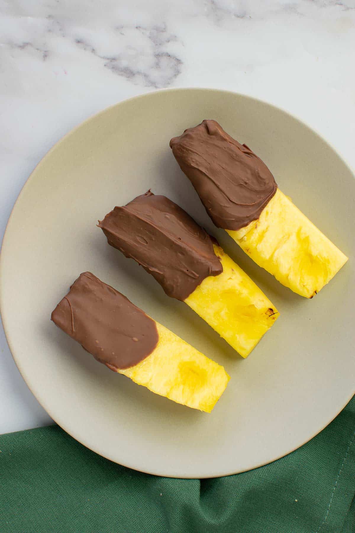 Chocolate dipped pineapple slices on a plate.