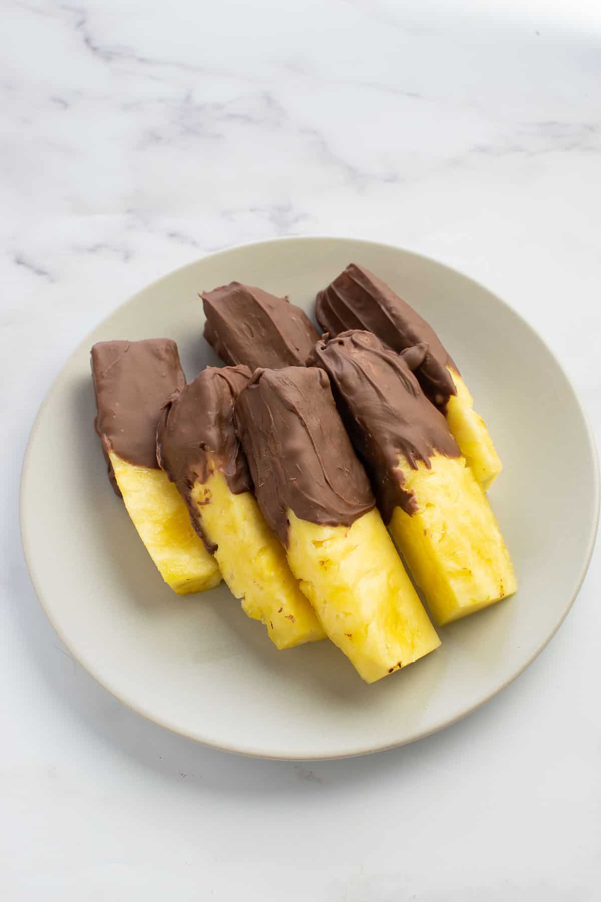 Chocolate covered pineapple sticks on a plate.