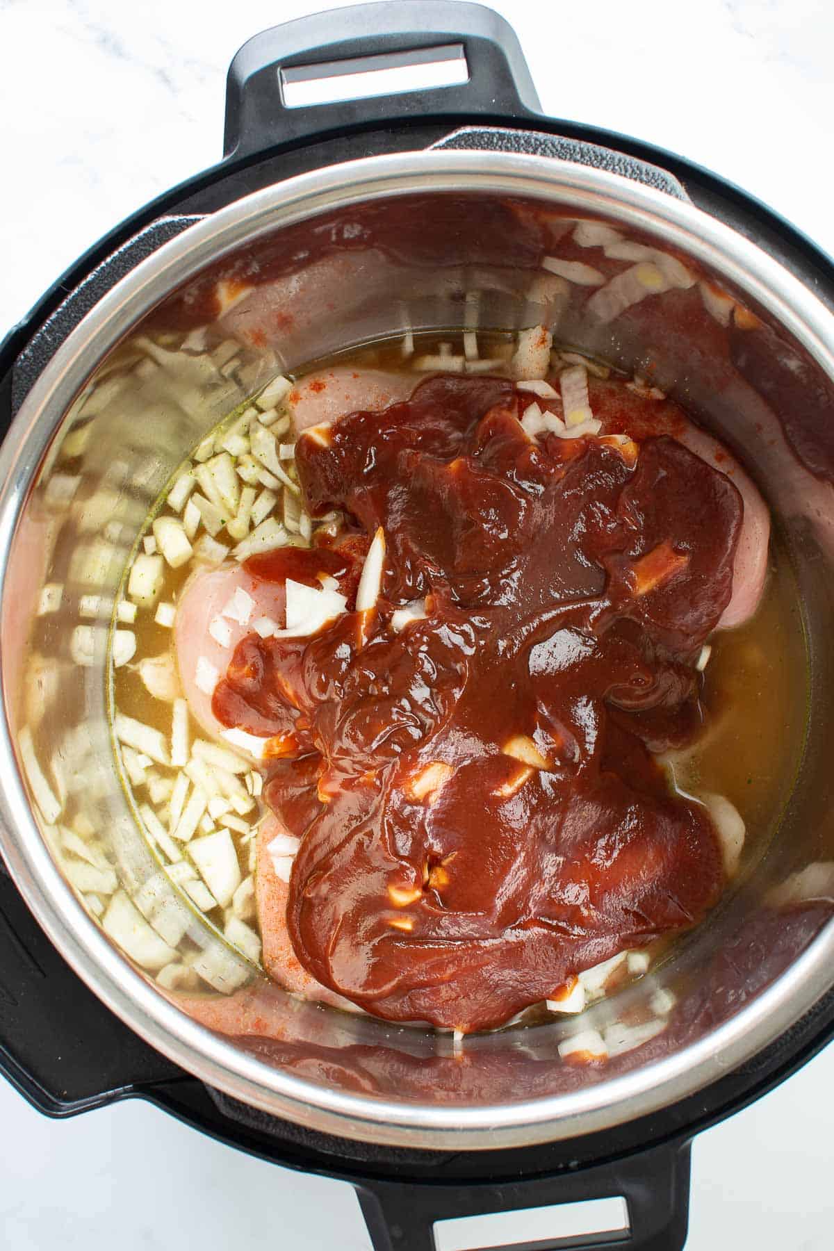 Chicken covered with onions and BBQ sauce in an instant pot.
