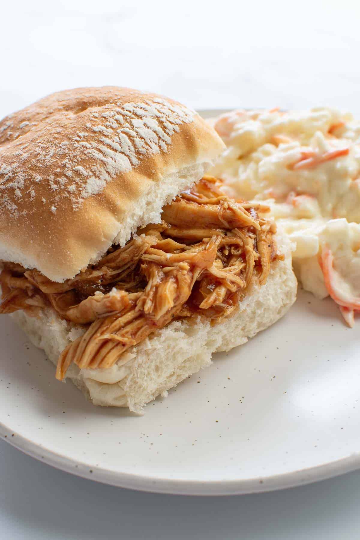 A shredded chicken slider with coleslaw on the side.