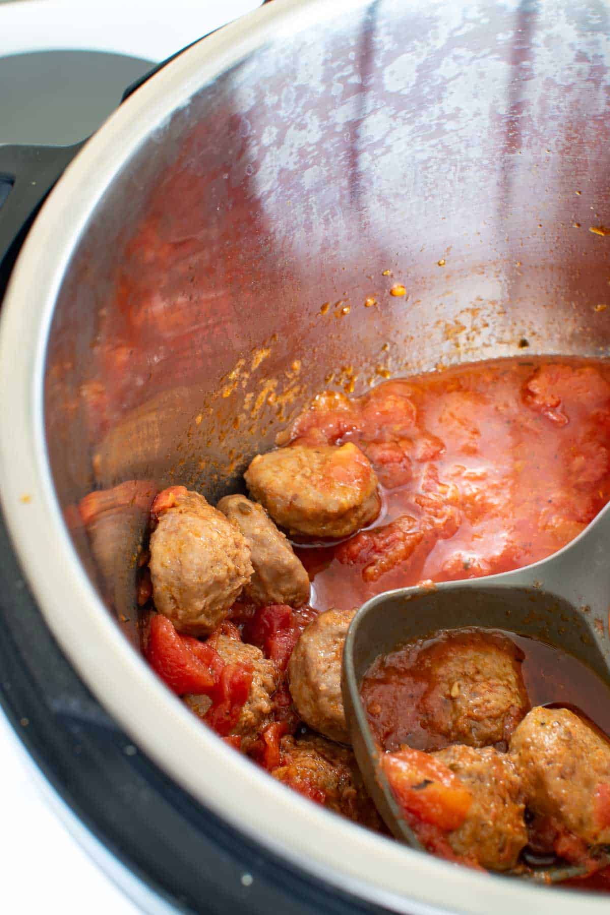 A ladle serving meatballs and tomato sauce from a pressure cooker.