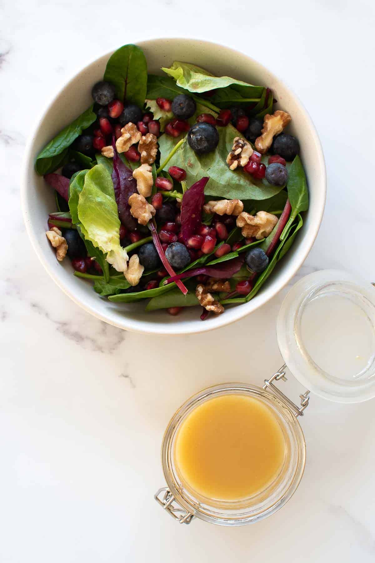 A bowl of salad, with maple syrup dressing on the side.