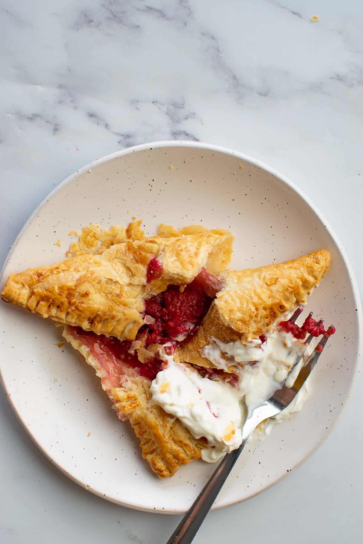 A raspberry pastry with cream that's been opened with a fork.