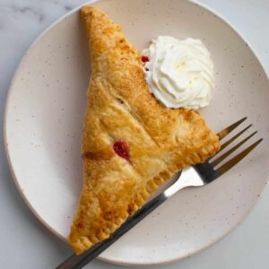 A raspberry turnover on a plate with whipped cream and a fork.